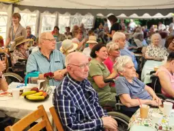 Grupa seniorów w trakcie wydarzenia na świeżym powietrzu, z uśmiechami i przekąskami na stole.