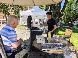 Mężczyzna grilluje jedzenie, a starszy pan obserwuje z miejsca siedzącego.