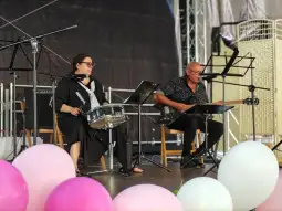 Muzycy grający na scenie, jeden na gitarze, drugi na perkusji, w otoczeniu balonów.