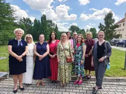 Grupa kobiet w eleganckich strojach na tle nieba z chmurami.