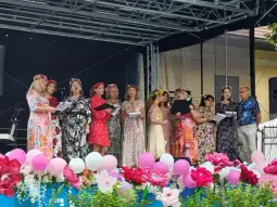 Grupa kobiet w kolorowych strojach śpiewa na scenie, otoczona kwiatami i balonami.