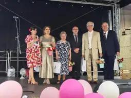 Grupa osób na scenie, trzymających kwiaty i uśmiechających się do publiczności.