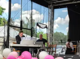 Muzyk grający na pianinie, dwóch mężczyzn siedzących obok, balony w różnych kolorach.