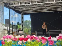 Występ artystki na scenie z pianistą, otoczony kwiatami i dekoracjami.