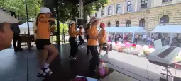 Grupa tancerzy w pomarańczowych koszulkach wykonuje układ taneczny na scenie.