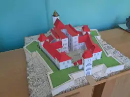 Model zamku z czerwonymi dachami i zielonym otoczeniem.