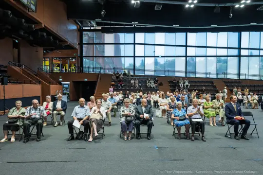 Grupa starszych osób siedzących na widowni w sali.