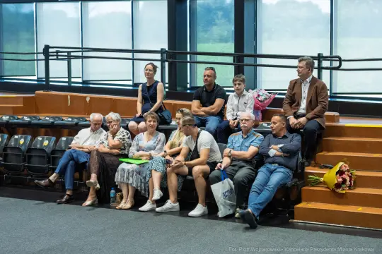 Grupa ludzi siedzących na widowni, niektórzy trzymają kwiaty.
