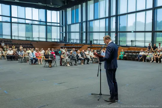 Mężczyzna przemawia do zgromadzonej publiczności w dużej sali.