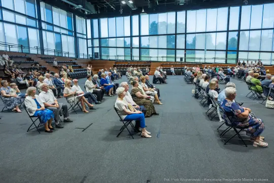 Grupa osób siedzących na krzesłach w dużej sali.