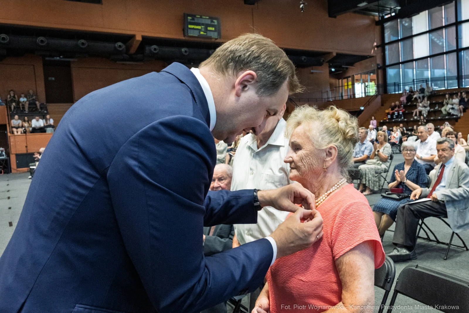 Wręczenie odznaczenia starszej kobiecie podczas uroczystości w sali.  Autor: Piotr Wojnarowski