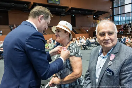 Uroczystość wręczenia odznaczeń, mężczyzna przypina medal do ubrania kobiety.