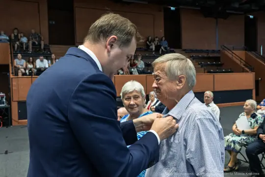 Wręczenie odznaczenia mężczyźnie przez uśmiechniętego mężczyznę w formalnym stroju.