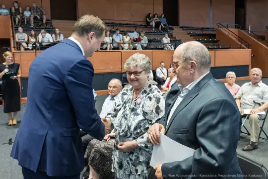 Uroczystość wręczenia odznaczeń, uśmiechnięci seniorzy w trakcie rozmowy z przedstawicielem władz.