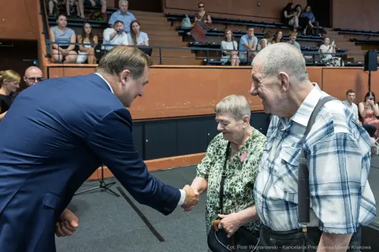 Spotkanie burmistrza z seniorami, uściski dłoni i uśmiechy.