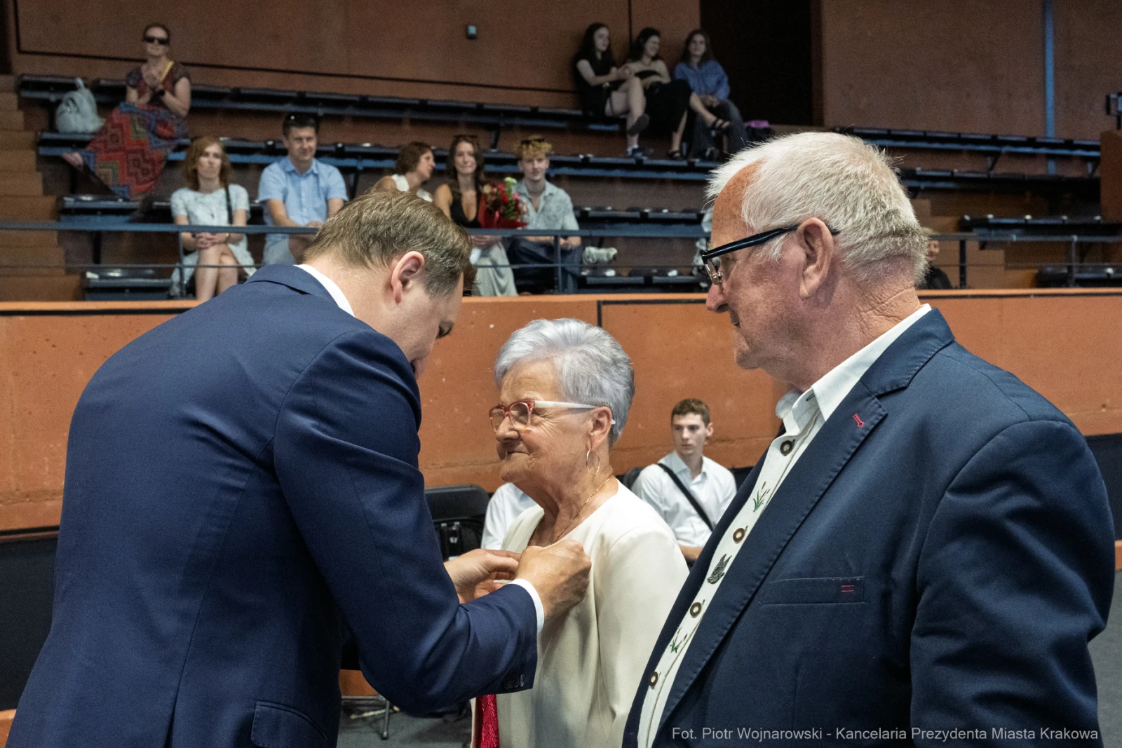 Wręczenie odznaczenia starszej kobiecie przez mężczyznę w garniturze, obok stoi drugi mężczyzna.  Autor: Piotr Wojnarowski
