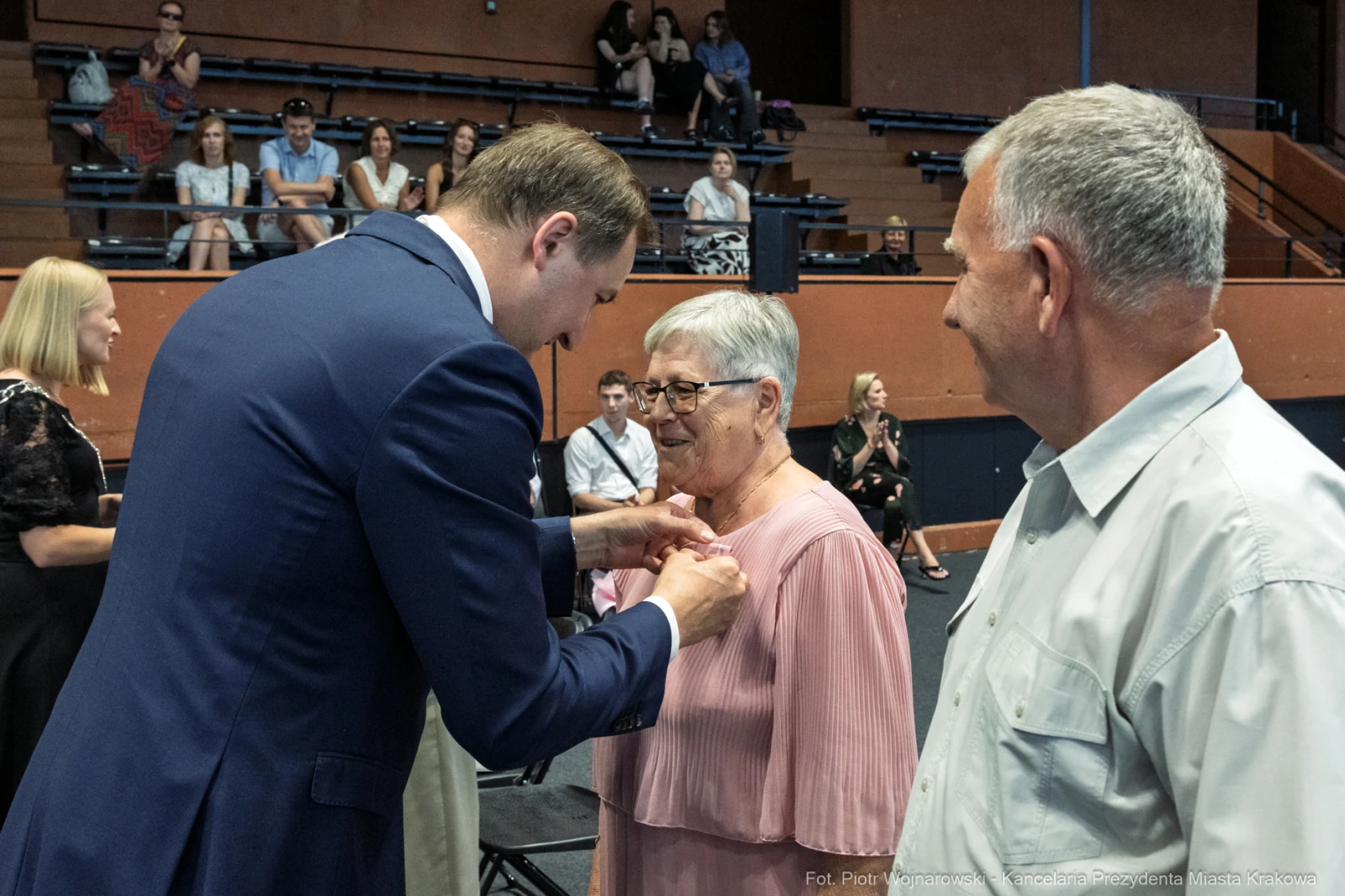 Wręczenie odznaczenia kobiecie przez mężczyznę w formalnym stroju, obok stoi inny mężczyzna.  Autor: Piotr Wojnarowski