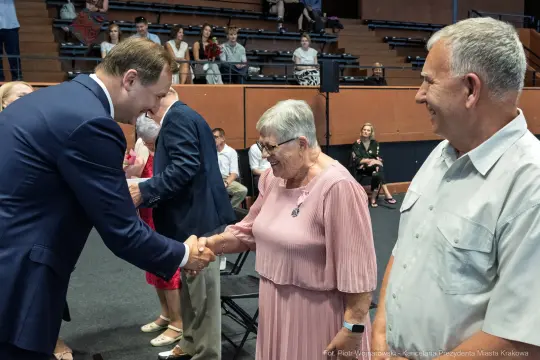 Uścisk dłoni między mężczyzną a starszą kobietą w sali z widownią.