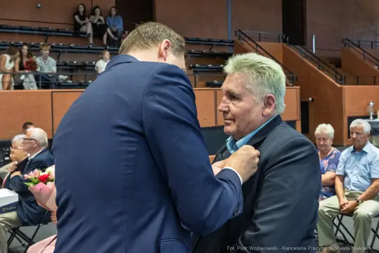 Mężczyzna odbiera odznaczenie podczas uroczystości w sali.