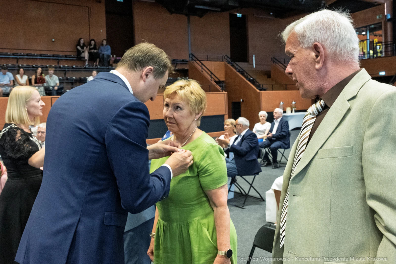 Uroczystość wręczenia odznaczeń, mężczyzna przypina medal kobiecie w zielonej sukience.  Autor: Piotr Wojnarowski
