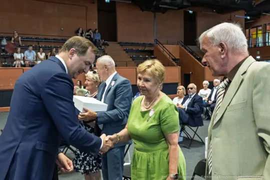 Uroczystość wręczenia nagród, ludzie w formalnych strojach, uściski dłoni.