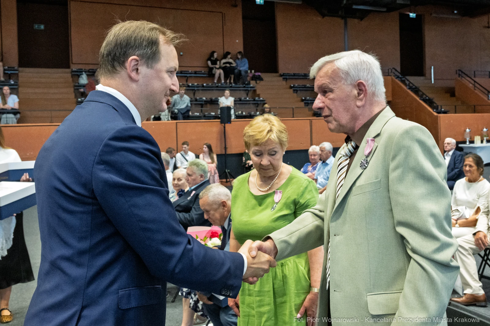 Uroczystość wręczenia odznaczeń, mężczyzna podaje rękę innemu mężczyźnie, w tle goście.  Autor: Piotr Wojnarowski