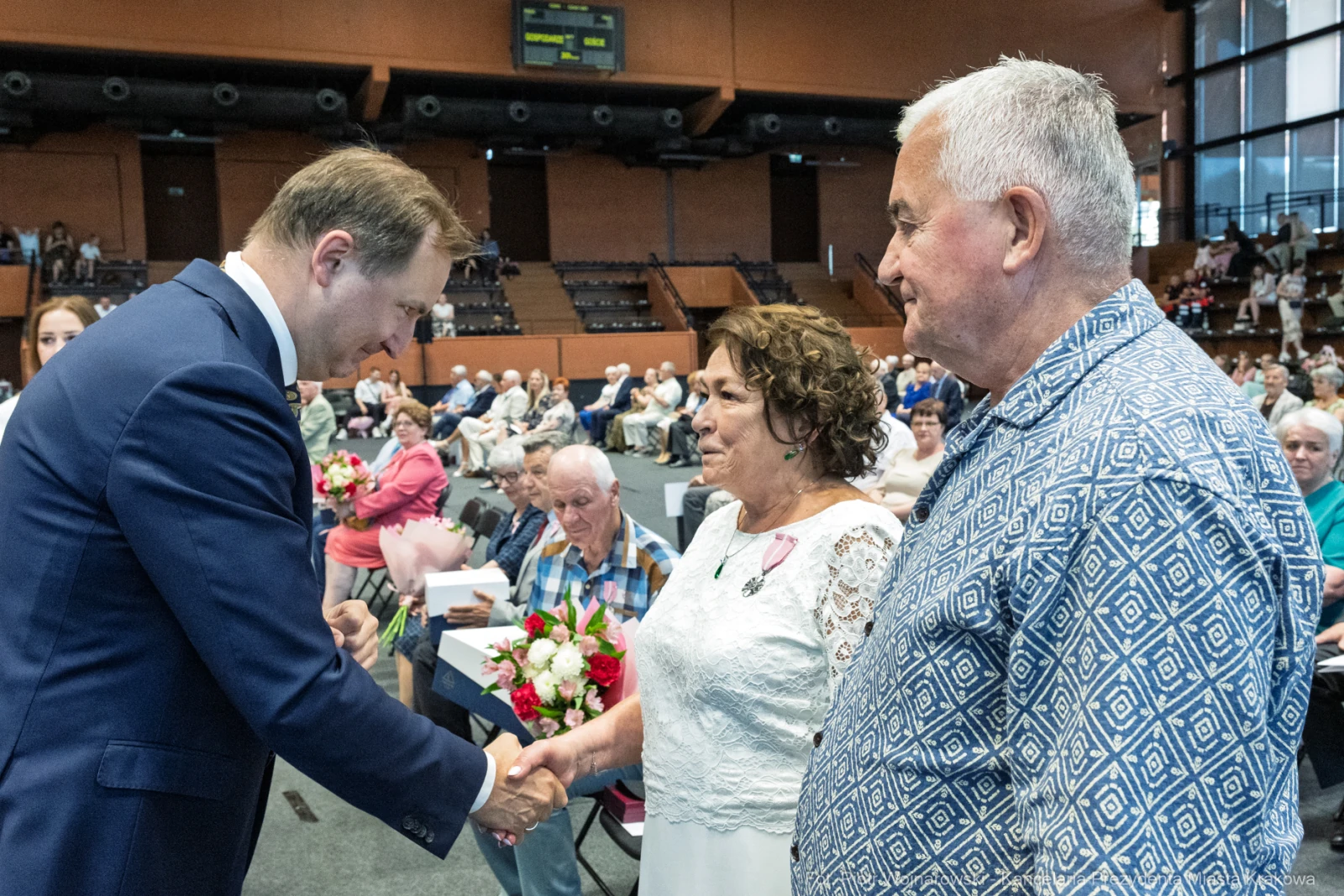 Uroczystość wręczenia odznaczeń, uściski dłoni, kwiaty w rękach.  Autor: Piotr Wojnarowski