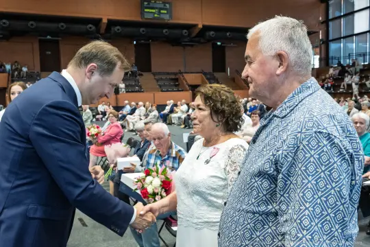 Uroczystość wręczenia odznaczeń, uściski dłoni, kwiaty w rękach.