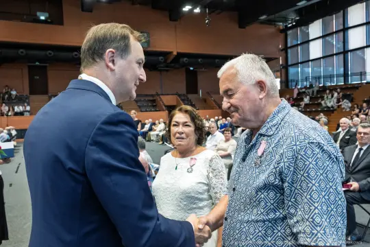 Wręczenie odznaczeń przez mężczyznę w garniturze, obok dwie osoby w eleganckich strojach.