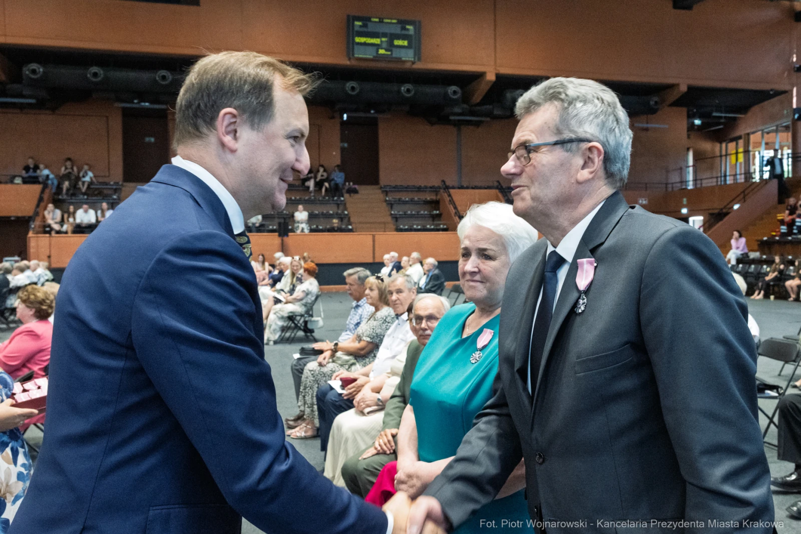 Mężczyźni w garniturach witają się, w tle siedzą goście w sali.  Autor: Piotr Wojnarowski