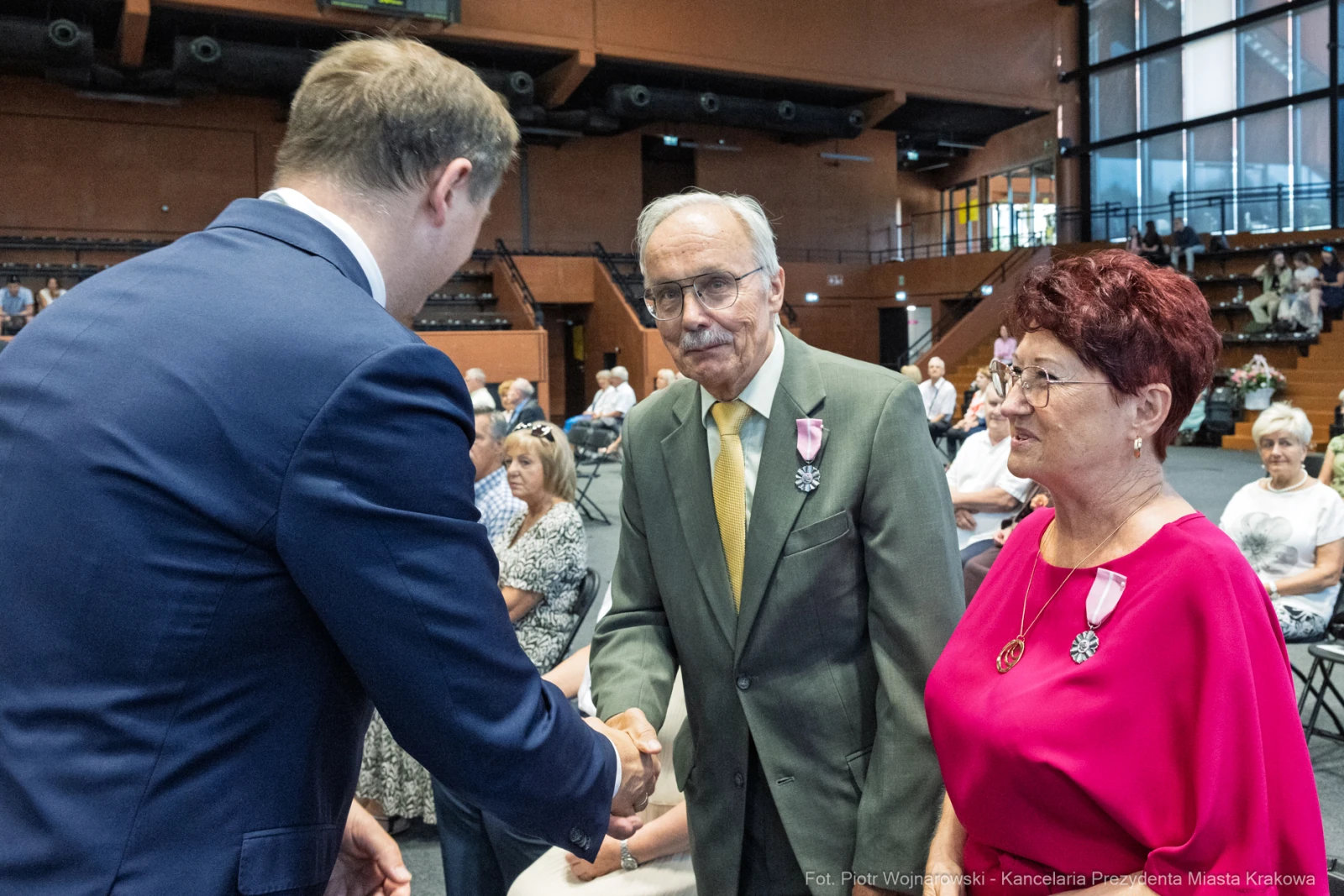 Uroczystość wręczenia odznaczeń, mężczyzna w garniturze podaje rękę starszemu mężczyźnie i kobiecie.  Autor: Piotr Wojnarowski