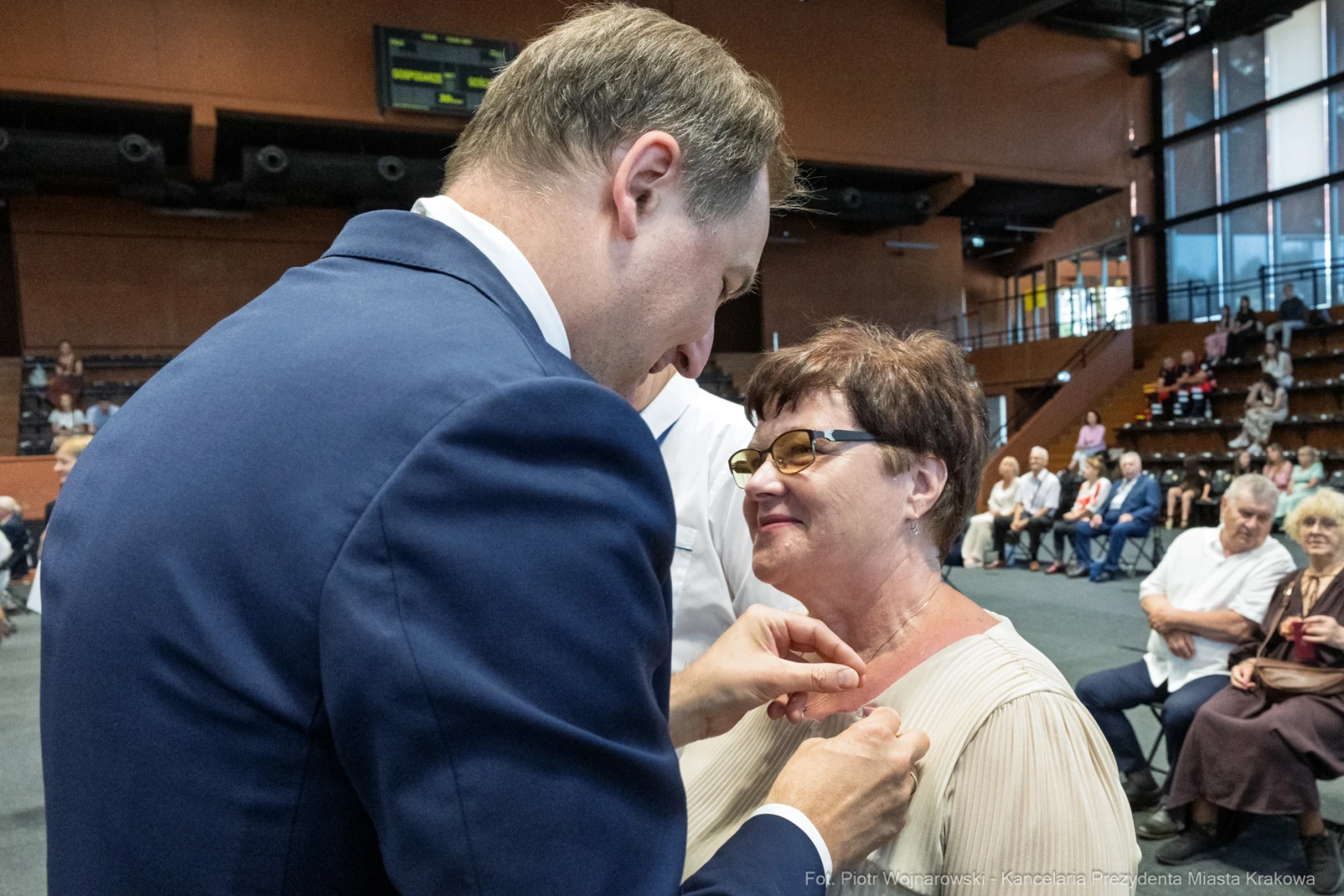 Uroczystość wręczenia odznaczenia przez mężczyznę kobiecie w eleganckim stroju.  Autor: Piotr Wojnarowski