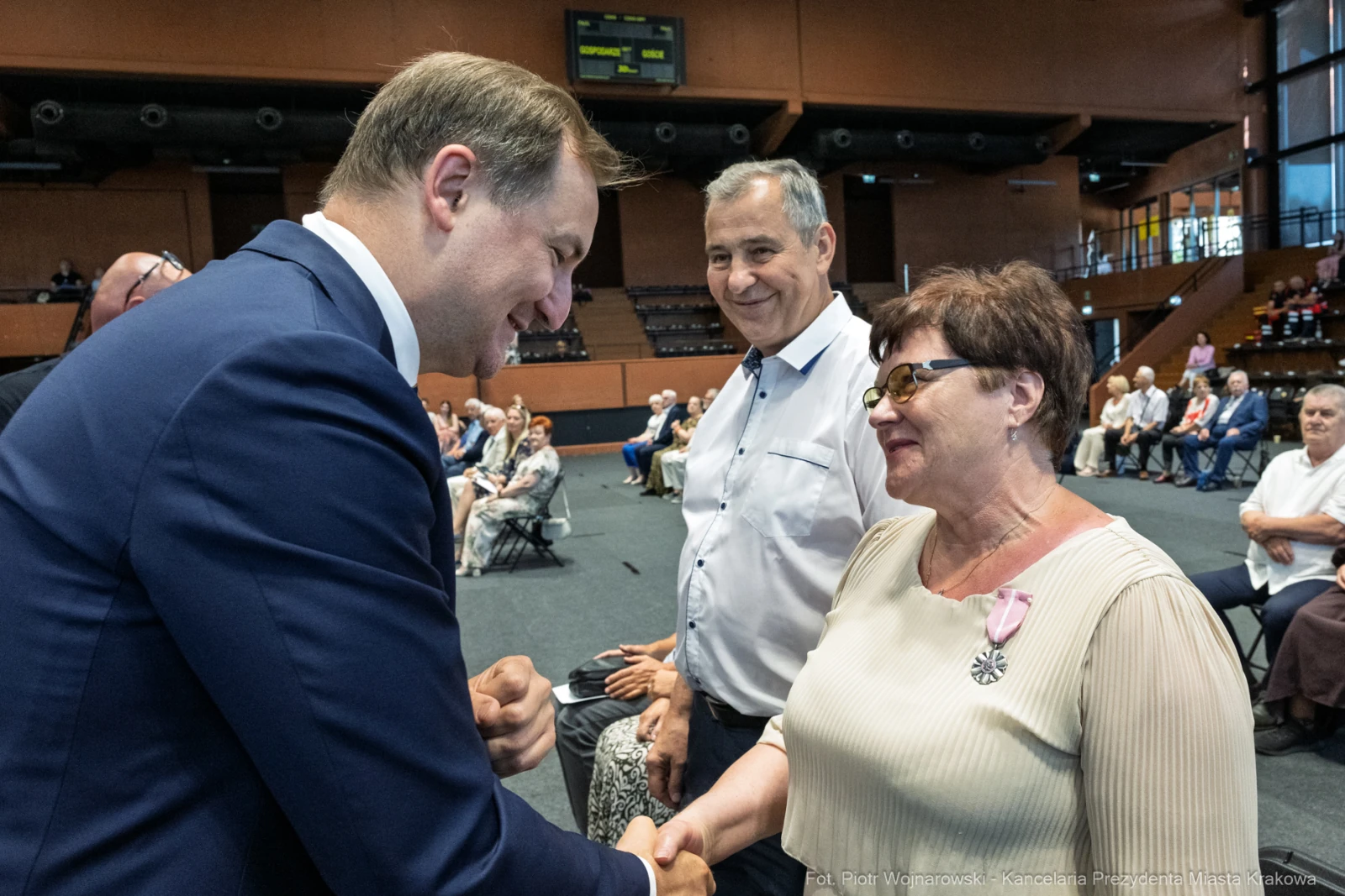 Spotkanie dwóch osób, uściski dłoni, uśmiechy, sala wypełniona ludźmi.  Autor: Piotr Wojnarowski