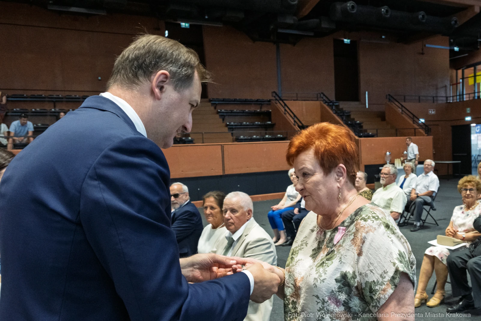 Wręczenie odznaczenia przez mężczyznę starszej kobiecie w sali z publicznością.  Autor: Piotr Wojnarowski