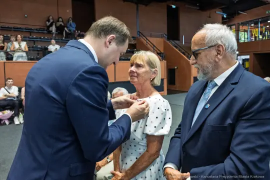 Wręczenie odznaczenia kobiecie przez mężczyznę w eleganckim garniturze.