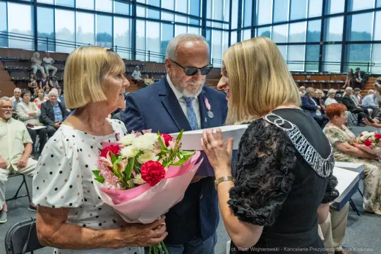 Uroczystość wręczenia nagród, osoby z kwiatami i w okularach przeciwsłonecznych.