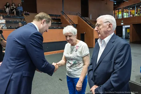 Spotkanie dwóch osób z mężczyzną w garniturze, uścisk dłoni.