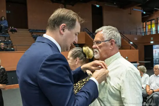Mężczyzna przypina odznaczenie innemu mężczyźnie podczas uroczystości.