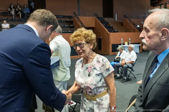 Spotkanie osób starszych z przedstawicielami władz, uściski dłoni i rozmowy.