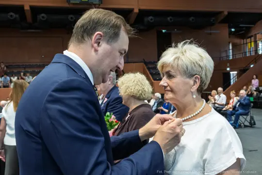 Uroczystość wręczenia odznaczeń, mężczyzna przypina medal kobiecie.