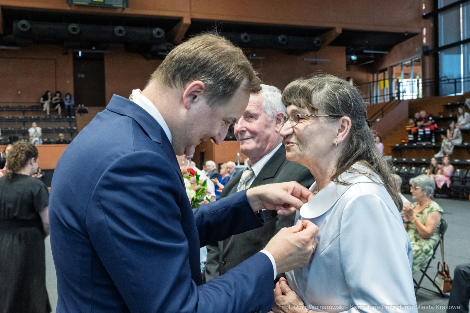 Mężczyzna przypina odznaczenie do ubrania kobiety w eleganckiej sali.  Autor: Piotr Wojnarowski