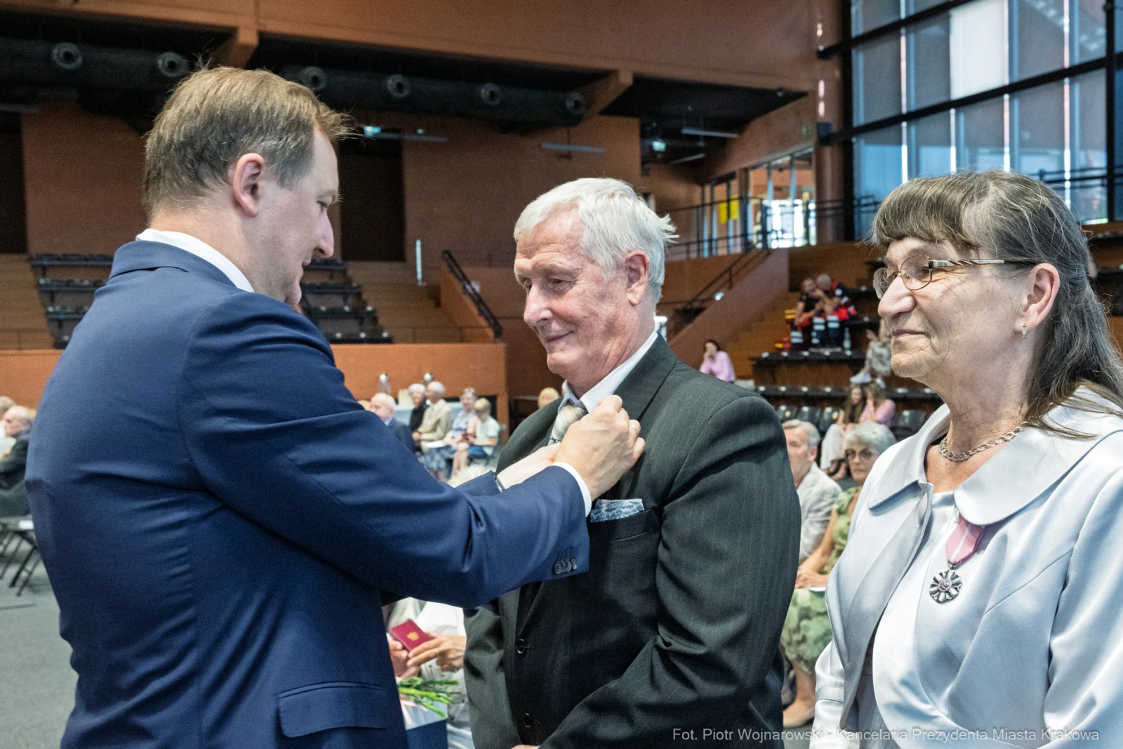 Uroczystość wręczenia odznaczeń, mężczyzna w garniturze z medalem, obok dwie osoby.  Autor: Piotr Wojnarowski