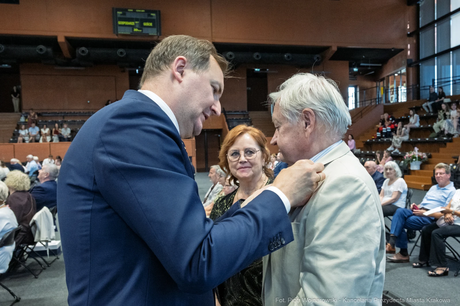 Uroczystość wręczenia odznaczeń, mężczyzna przypina medal starszemu mężczyźnie, obok kobieta.  Autor: Piotr Wojnarowski