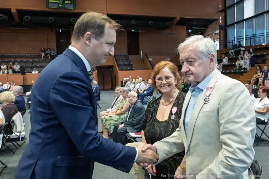 Uroczystość wręczenia odznaczeń, uściski dłoni i uśmiechy uczestników.