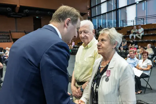 Wręczenie odznaczeń przez mężczyznę w garniturze dwóm starszym osobom.
