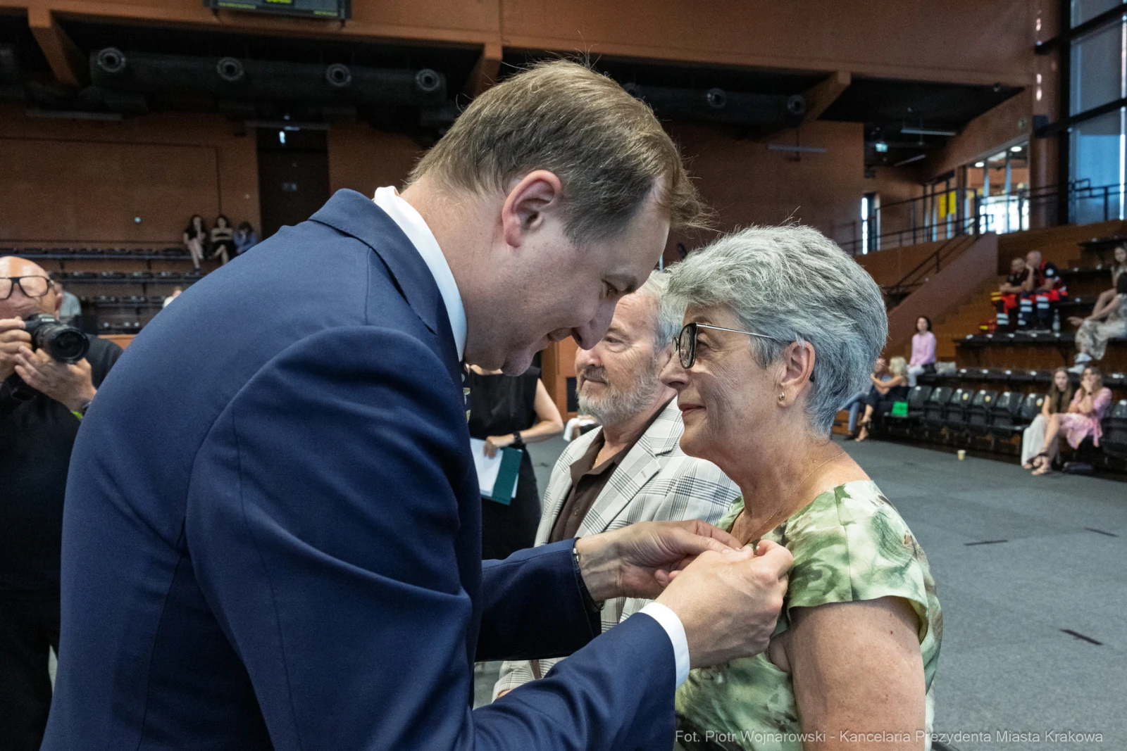 Wręczenie odznaczenia przez mężczyznę starszej kobiecie w towarzystwie innego mężczyzny.  Autor: Piotr Wojnarowski