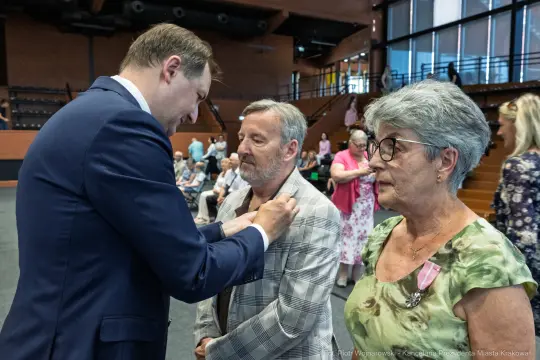 Uroczystość wręczenia odznaczeń, mężczyzna przypina medal do marynarki innego mężczyzny.