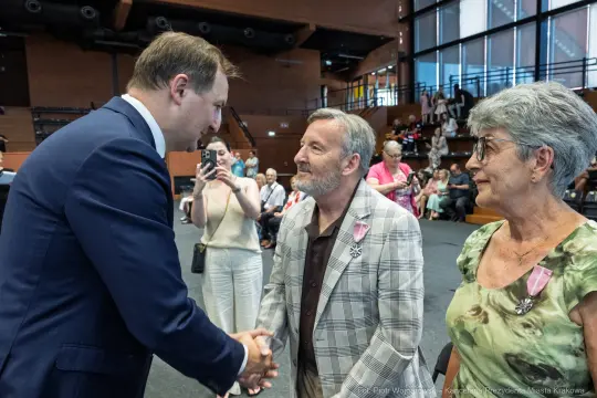 Spotkanie trzech osób, w tym mężczyzny w garniturze, w sali z widownią.