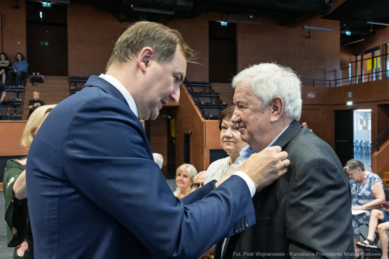 Mężczyzna przypina odznaczenie innemu mężczyźnie w towarzystwie osób w tle.  Autor: Piotr Wojnarowski