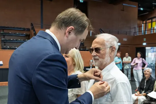 Mężczyzna przypina odznaczenie starszemu mężczyźnie w trakcie uroczystości.